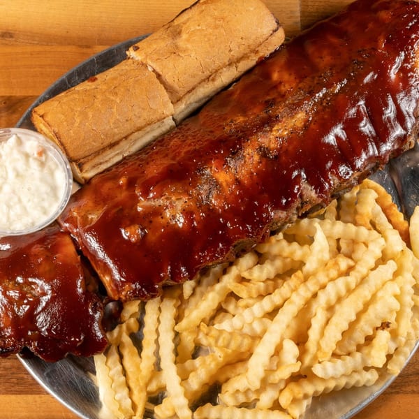 A full rack of BBQ ribs, crinkle-cut fries, and bread on a metal platter.