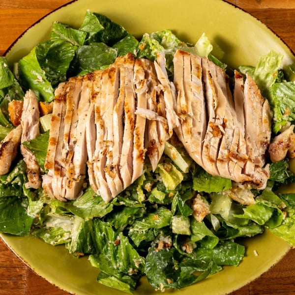 Grilled chicken Caesar salad with crisp romaine lettuce, croutons, and creamy dressing on a green plate.